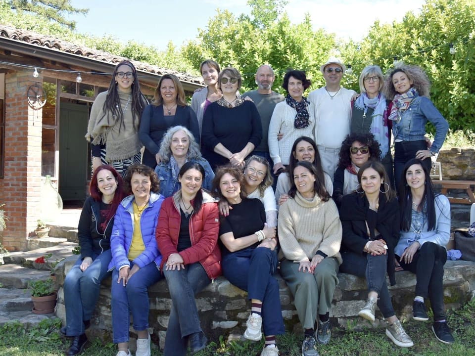 Un grande gruppo di partecipanti riunito davanti a una casa di campagna, durante un incontro all’aperto.